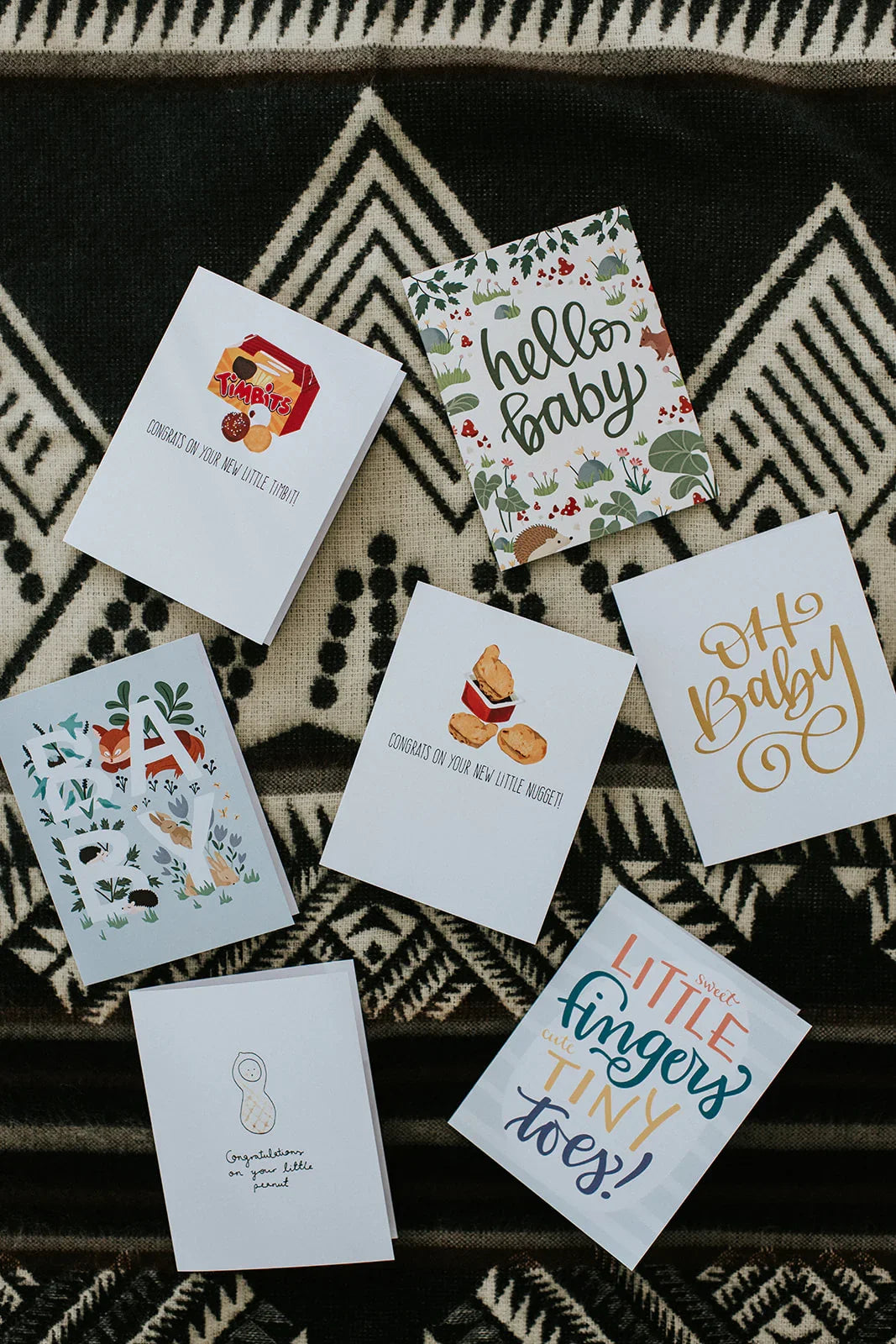 Assorted baby greeting cards with playful designs on a black and white patterned fabric.