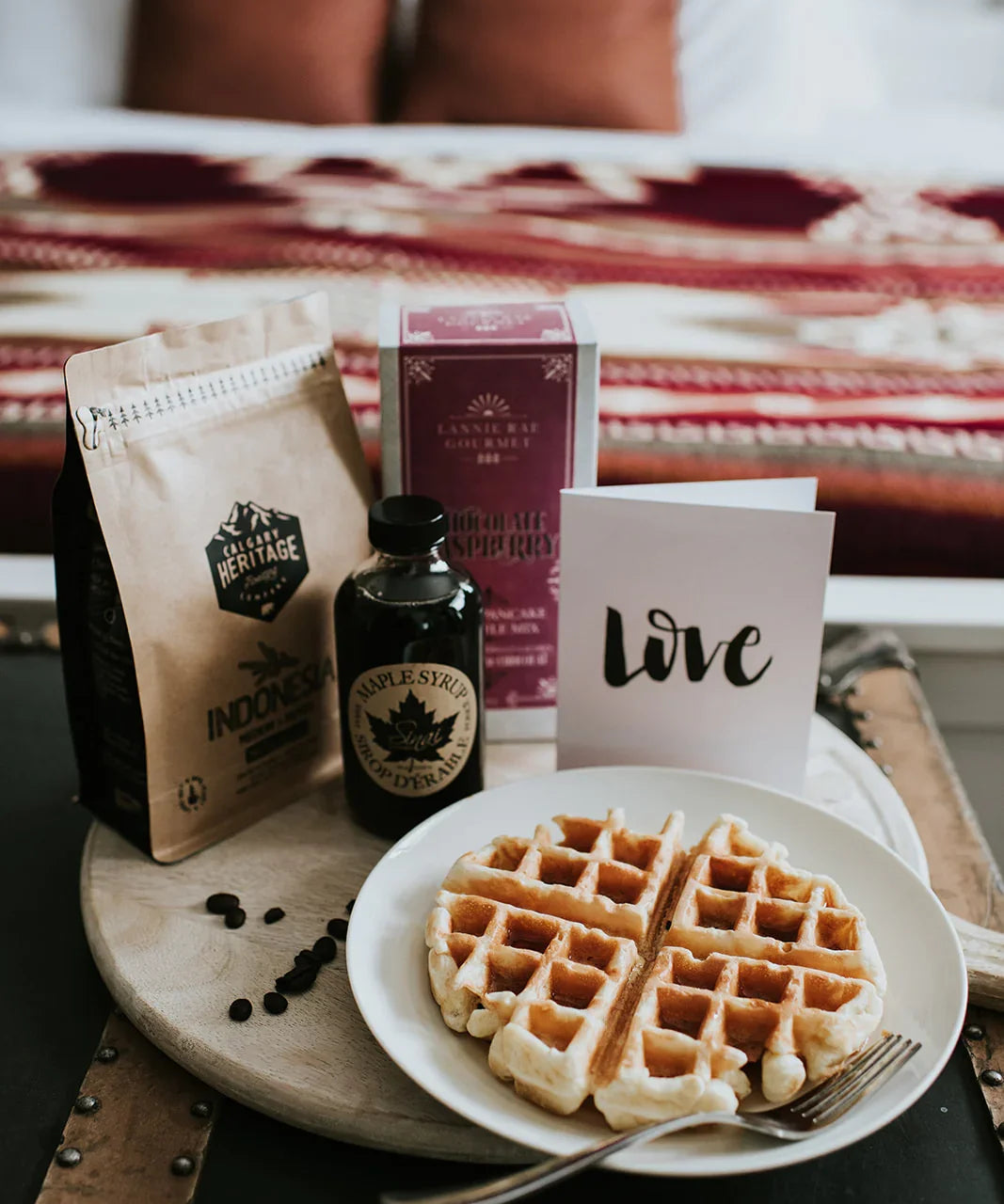 Breakfast in bed with waffles, maple syrup, coffee, and decorative red throw blanket