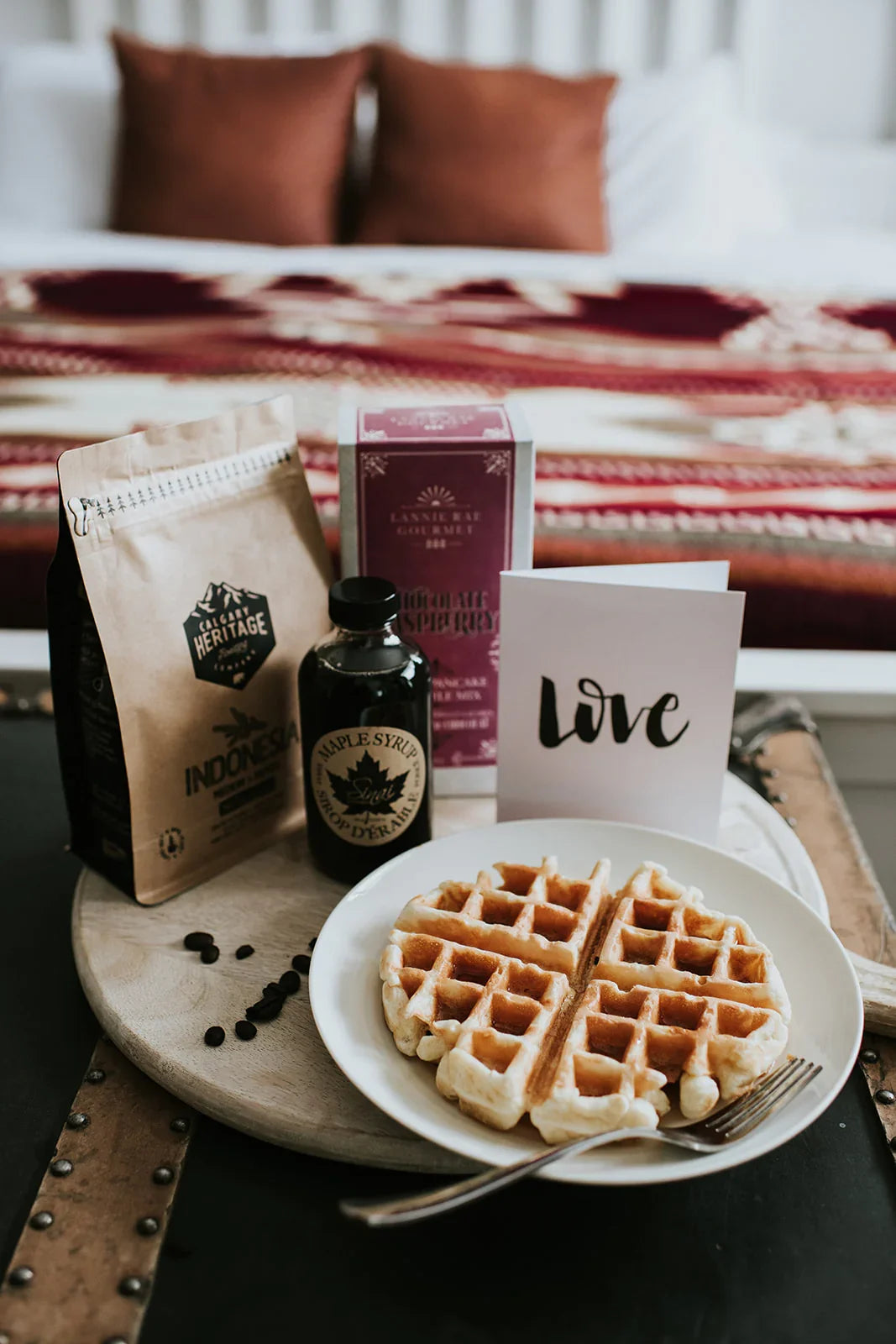 Breakfast in bed with waffles, maple syrup, coffee, and decorative red throw blanket
