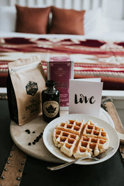 Breakfast in bed with waffles, maple syrup, coffee, and decorative red throw blanket