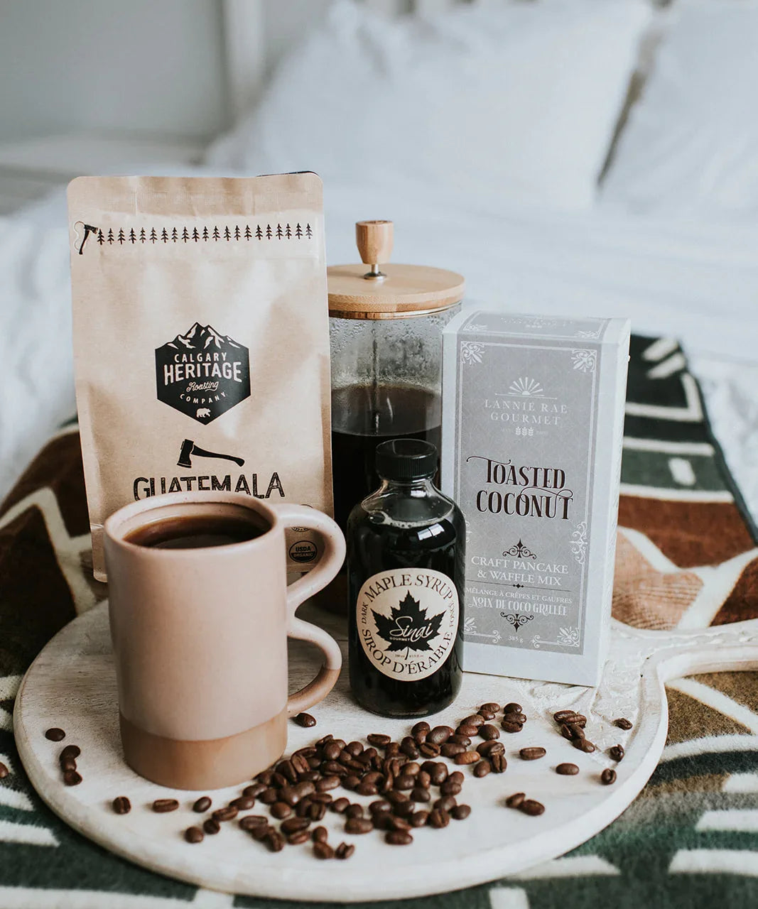 Coffee, maple syrup, pancake mix, and mug on a tray atop a cozy patterned blanket