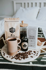 Coffee, maple syrup, pancake mix, and mug on a tray atop a cozy patterned blanket