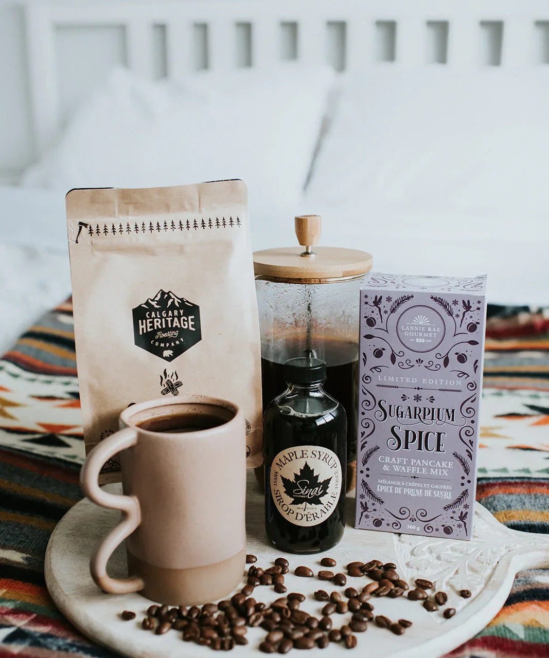 Cozy breakfast setup with coffee, maple syrup, pancake mix and coffee beans on patterned blanket
