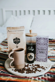 Cozy breakfast setup with coffee, maple syrup, pancake mix and coffee beans on patterned blanket