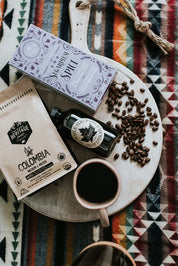 Coffee beans, Colombian coffee, maple syrup, and spiced pancake mix on a serving board over a patterned blanket