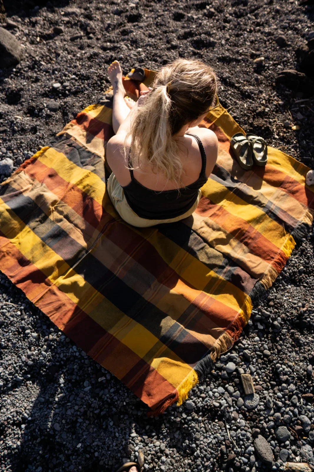 Woman sitting on a striped blanket with warm tones on rocky ground outdoors