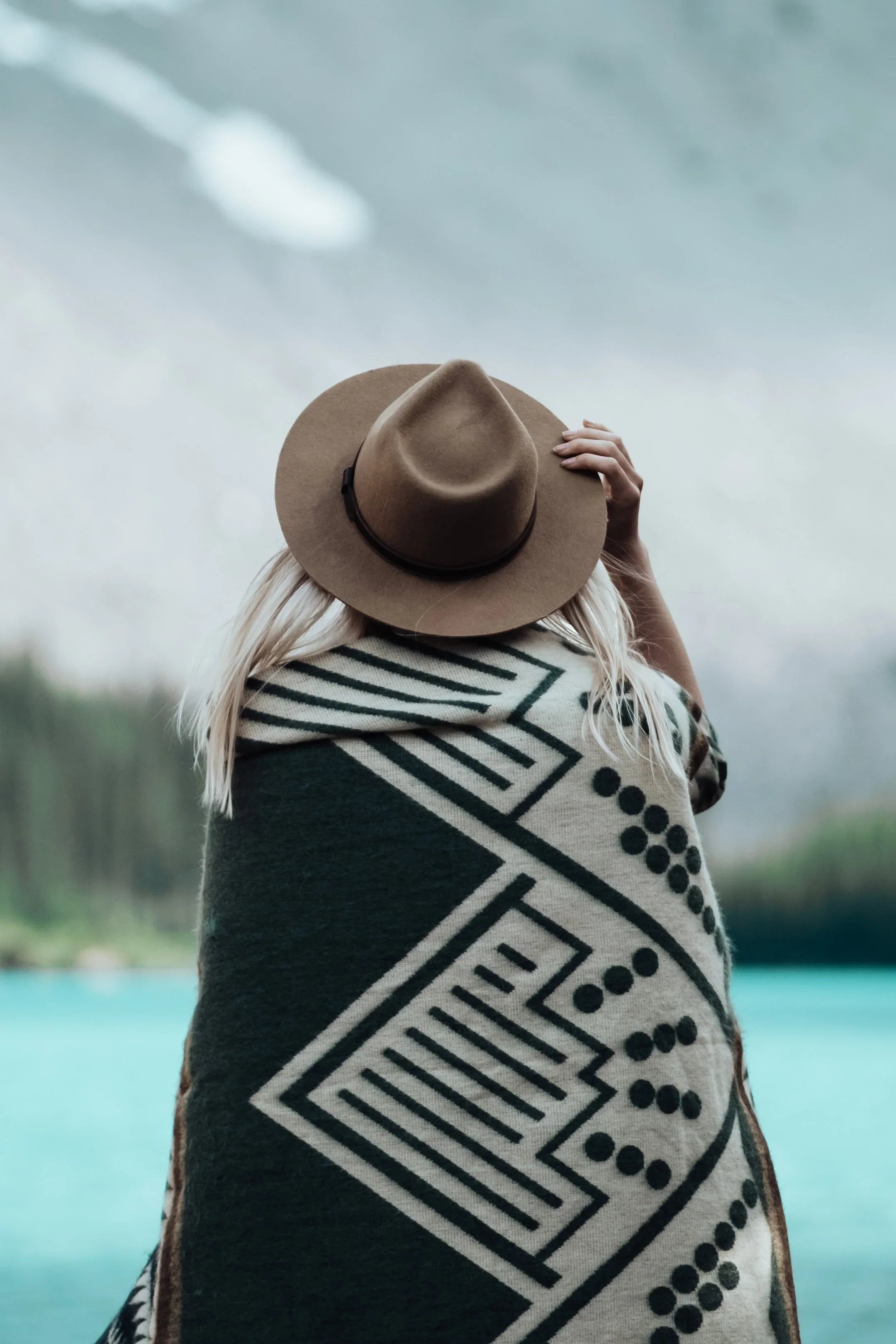 Woman in patterned blanket and hat by mountain lake outdoors